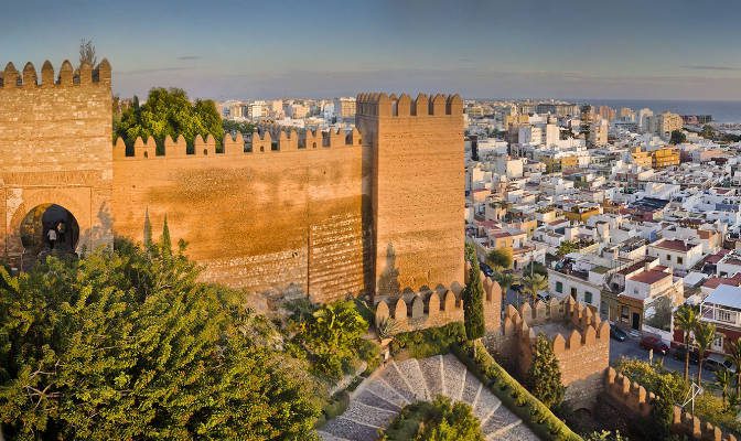 Walls and towers of the Alcazaba of Almería, with the whitewashed city and the Mediterranean Sea in the background.