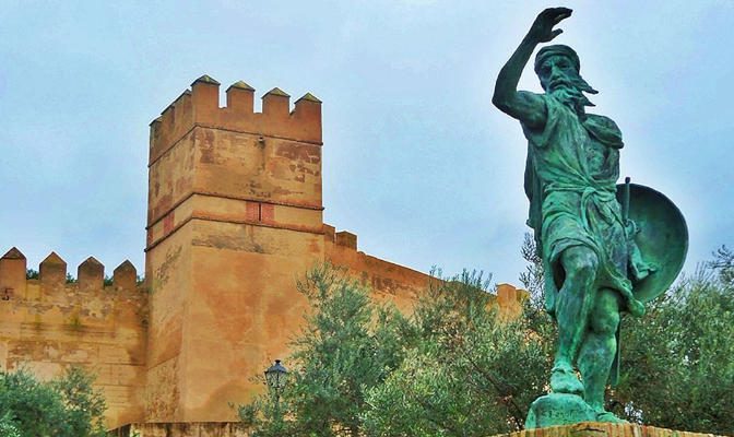 Monument to Ibn Marwan, founder of Badajoz, silhouetted against the historic walls of the Alcazaba of Badajoz in Extremadura, Spain.