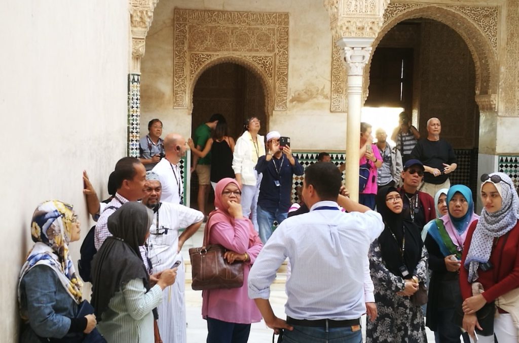 Group of Muslim travelers listening attentively to their tour guide during a visit to the Alhambra in Granada, Spain.
