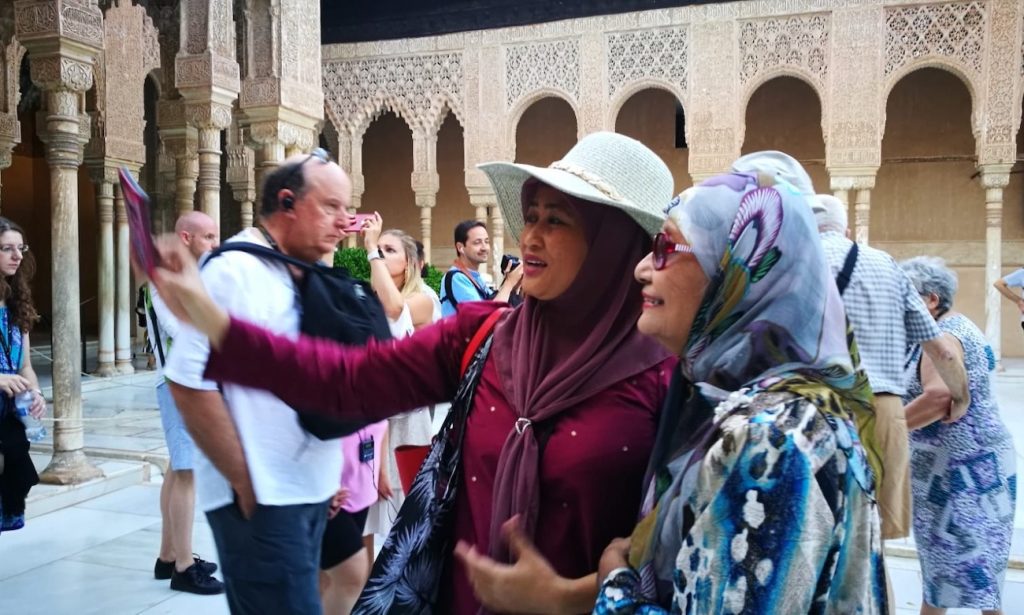Two Muslim women in the foreground visiting the Nasrid Palaces of the Alhambra in Granada.