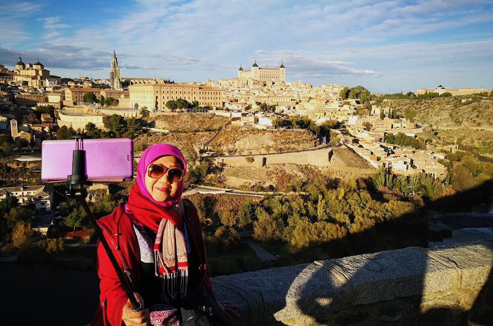 Muslim woman taking a selfie with a panoramic view of Toledo's historic city in the background.